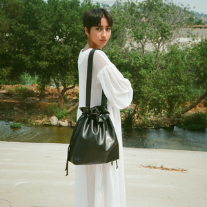 Large vegan leather shoulder tote in black with black strap and string closure.  Model wears the bag over her shoulder.