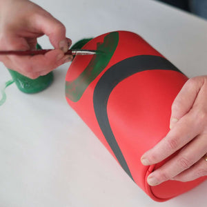 Vegan leather duffle style mini bag with detachable crossbody strap in red with hand painted squiggles in black and green.  Artist in the process of painting the bag.