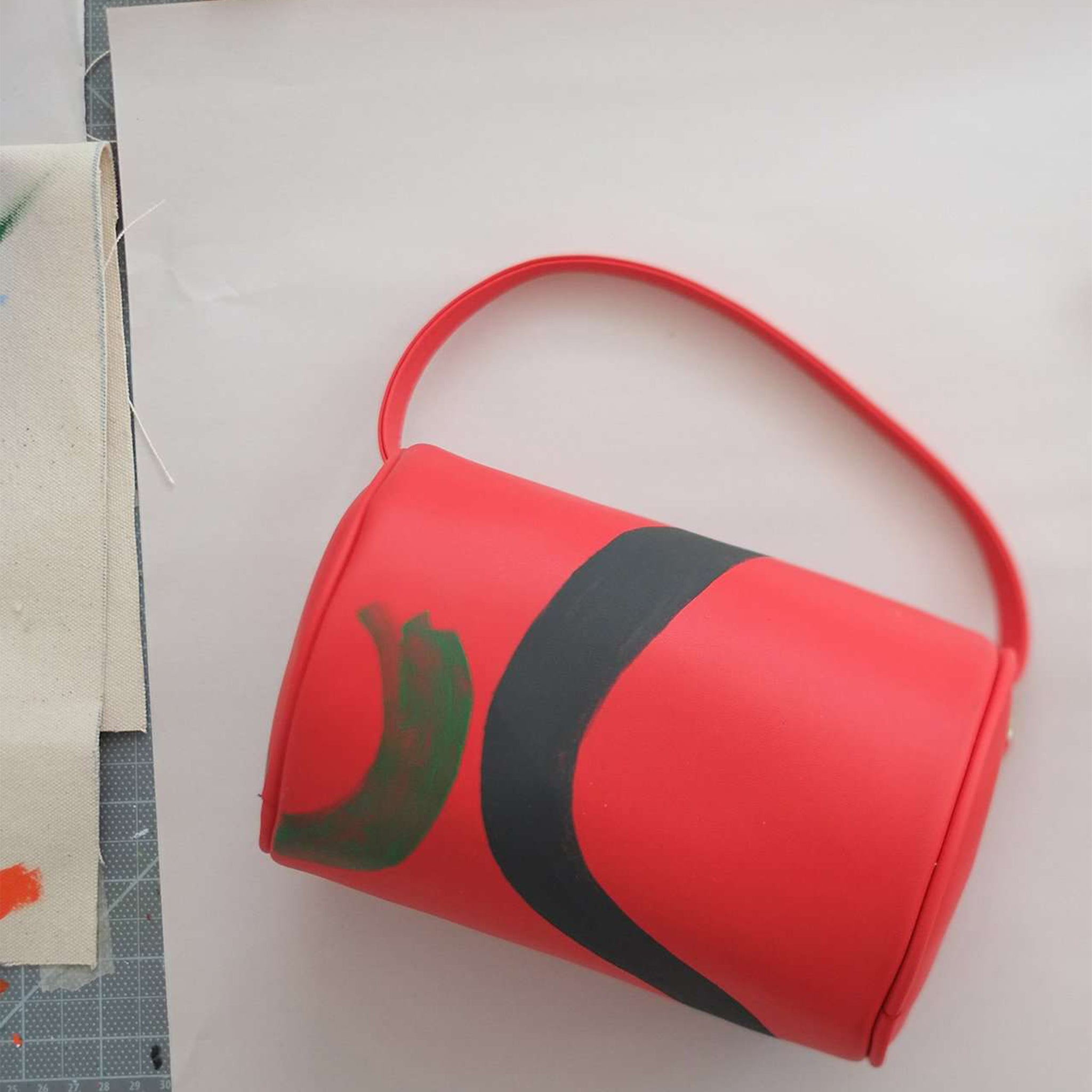 Vegan leather duffle style mini bag with detachable crossbody strap in red with hand painted squiggles in black and green.  Overhead shot.