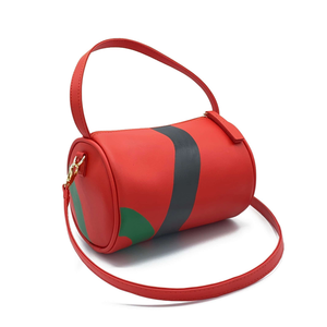 Vegan leather duffle style mini bag with detachable crossbody strap in red with hand painted squiggles in black and green.  3/4 angle shot featuring crossbody strap.